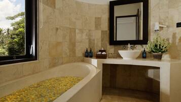 A bathroom with a freestanding bathtub, a sink with a mirror above it, and a window with a view of greenery.