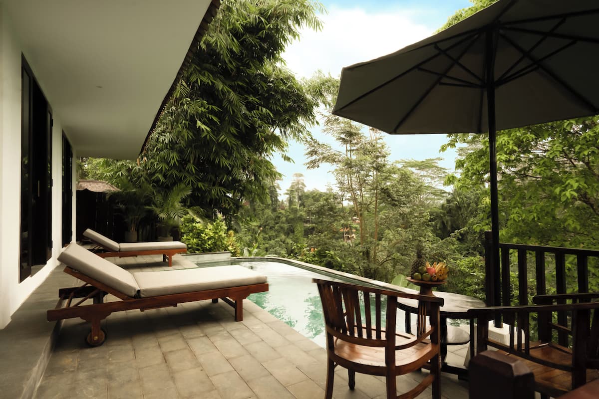 A poolside area with lounge chairs, a table with a fruit bowl, and a large umbrella.