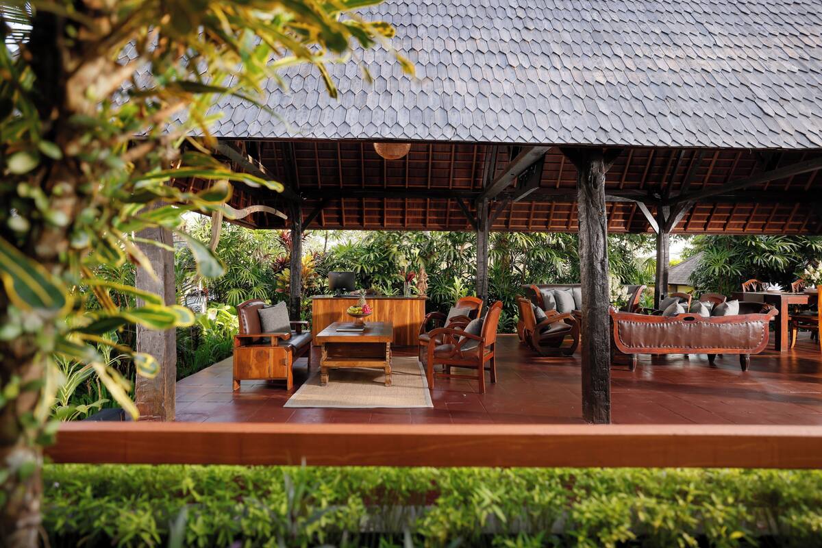 An outdoor seating area with wooden furniture, a hanging basket, and lush greenery.