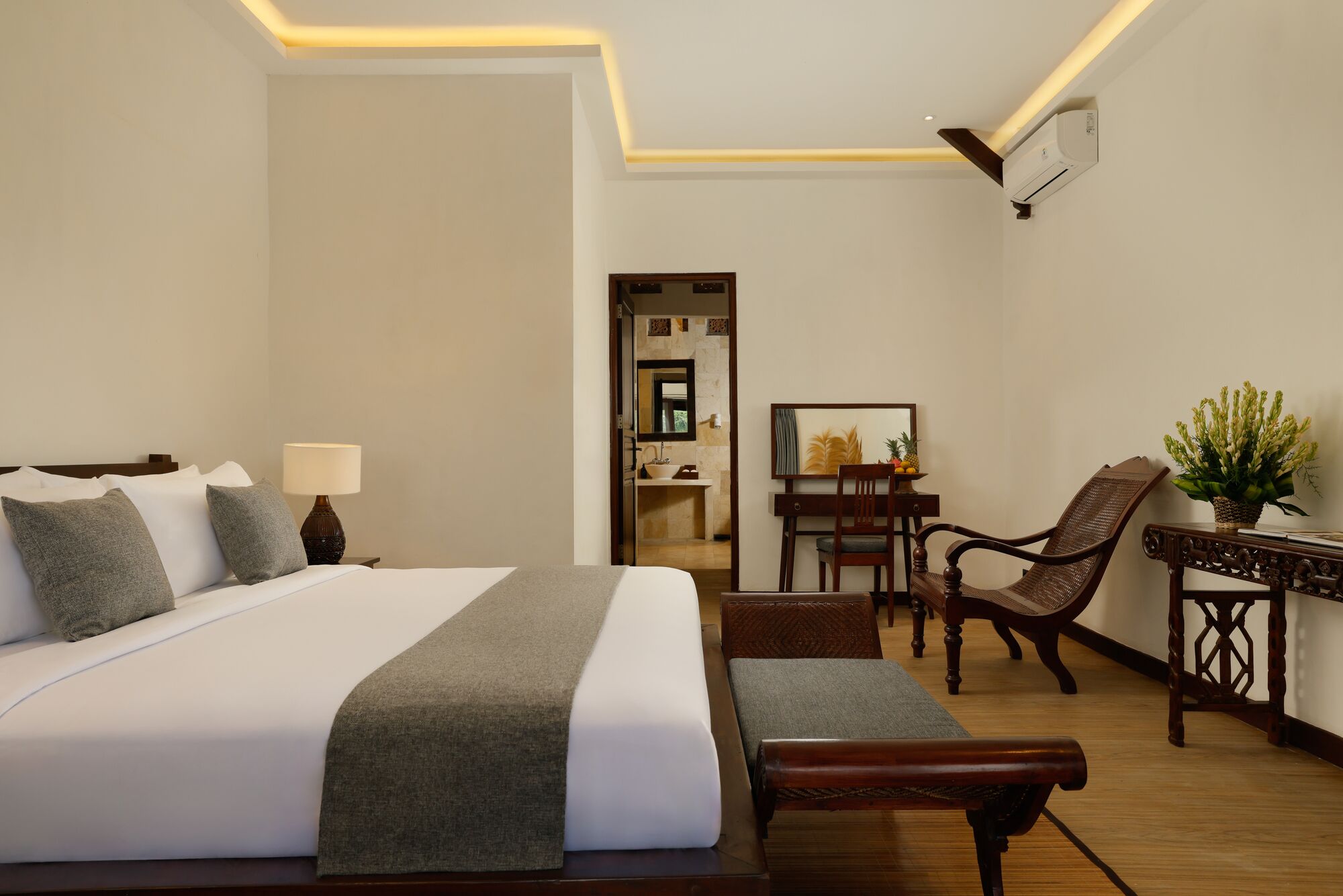 A hotel room with a large bed, bedside table, lamp, chair, desk, and potted plant.