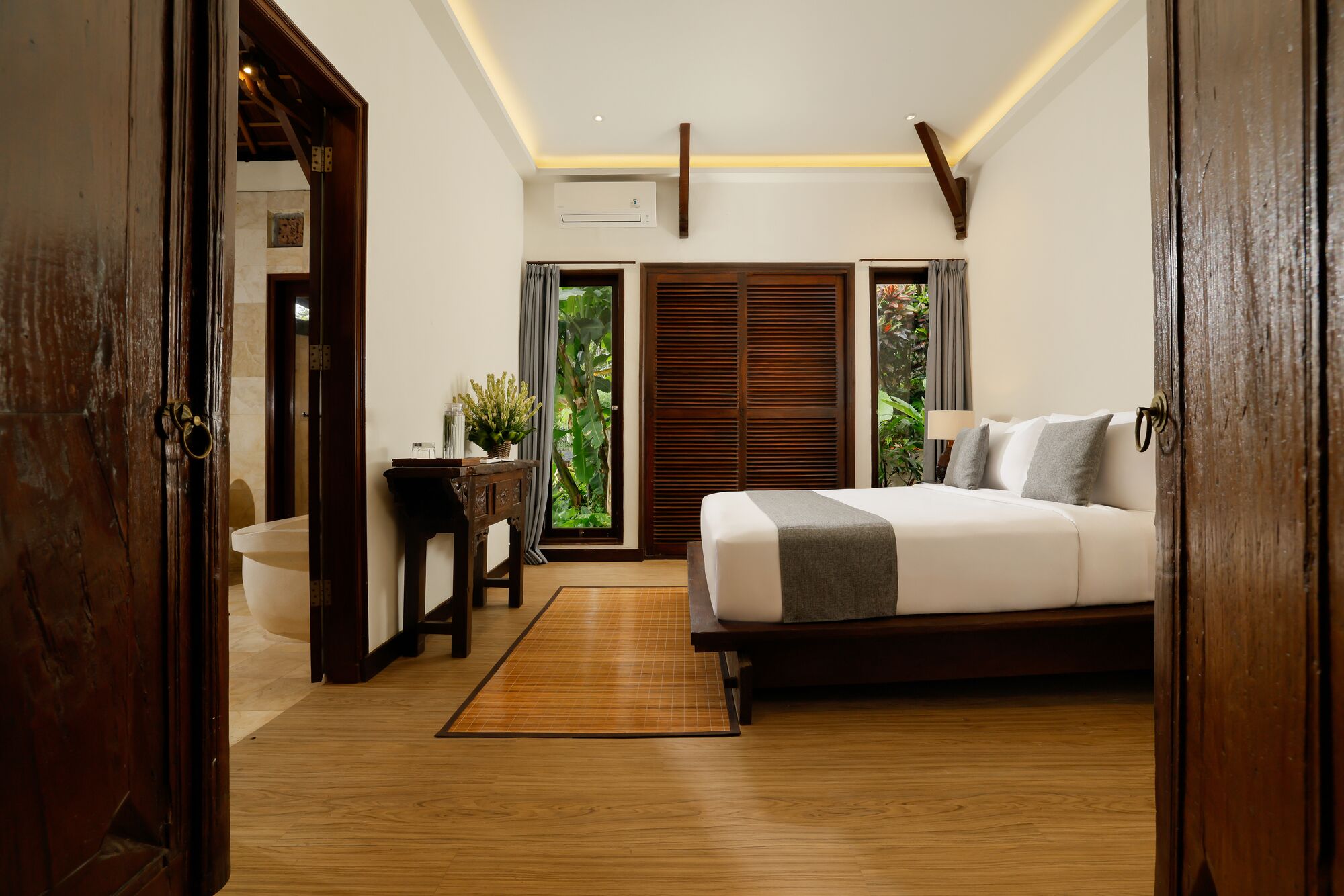 A bedroom with a bed, bedside table, and a view of greenery through the window.