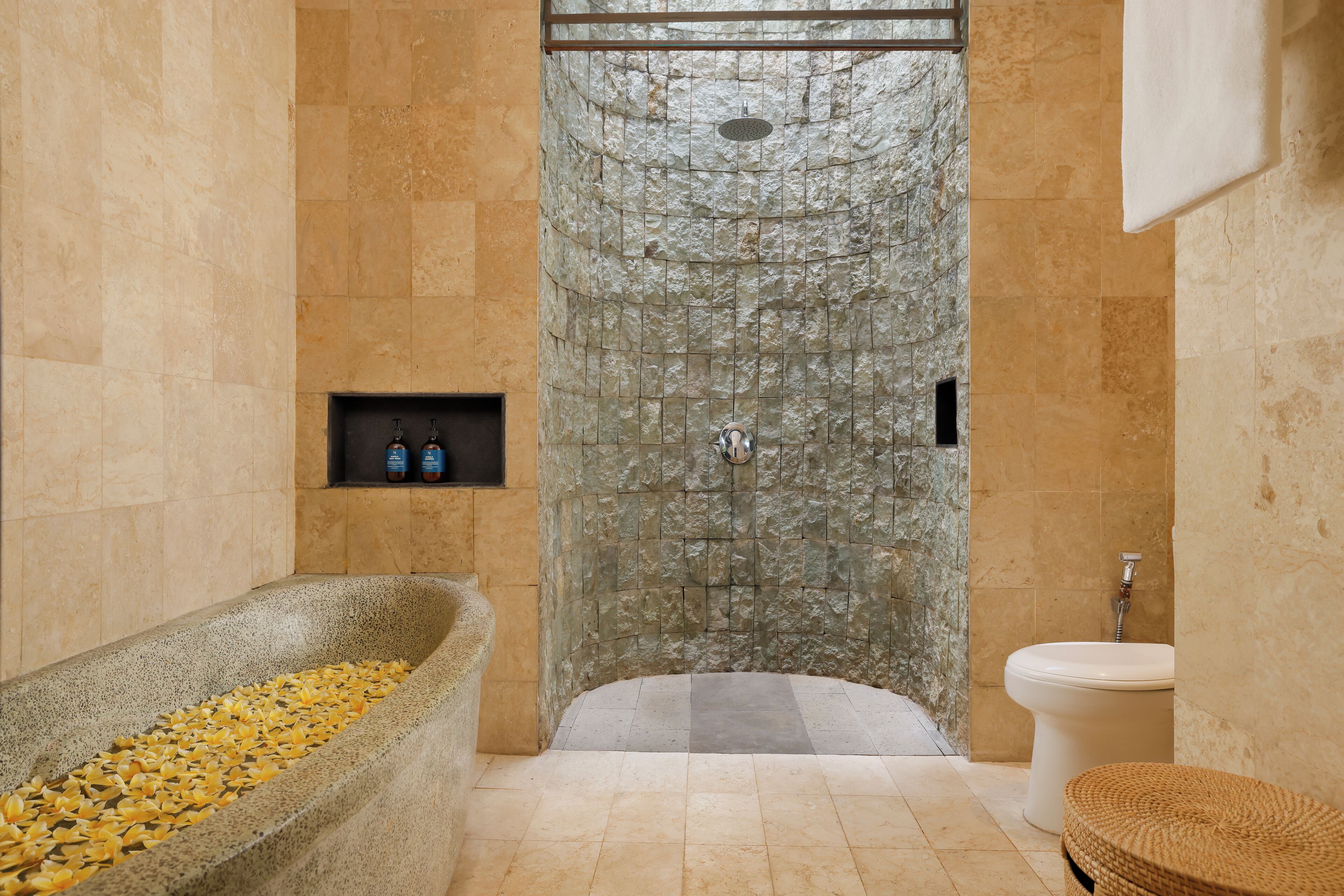 A bathroom with a stone shower, a bathtub filled with yellow flowers, and a toilet.
