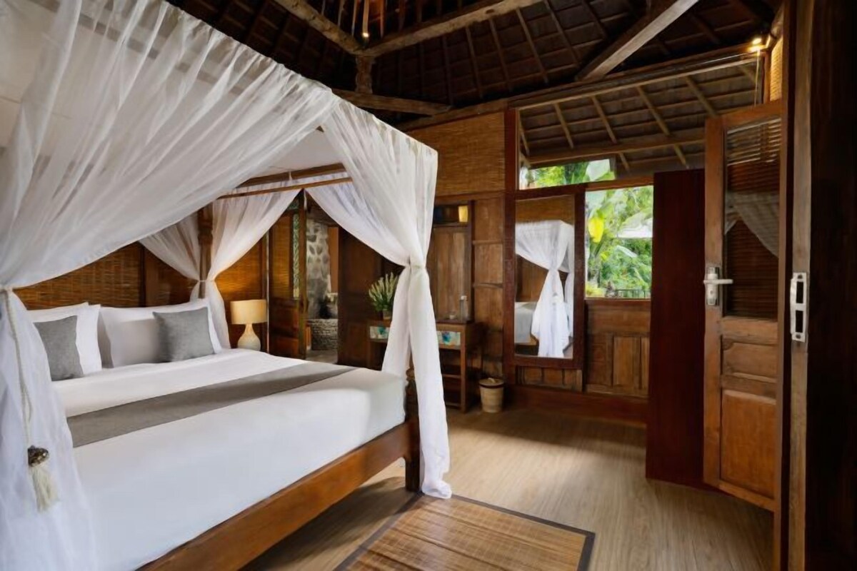 Habitación con cama bajo un dosel, paredes de madera y vistas a la vegetación exterior.