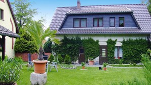 Una casa de dos pisos con techo inclinado, un jardín delantero con plantas en macetas y un estanque pequeño.