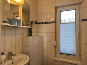 Un baño con lavabo, espejo y ventana con persianas.
