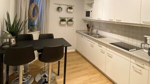 A modern kitchen with white cabinets, a stainless steel sink, and a dining area with a table and chairs. - Ferienwohnung, St. Peter - Ording (St. Peter-Ording)