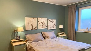 A bedroom with a bed, two nightstands, a window with curtains, and three wall-mounted floral artworks. - Ferienwohnung, St. Peter - Ording (St. Peter-Ording)