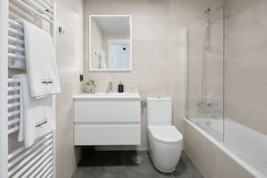 Un baño moderno con un tocador blanco, inodoro, cabina de ducha y un perchero con toallas.