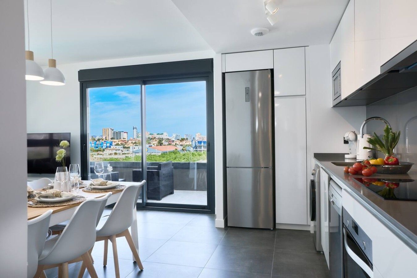 A modern kitchen with a large refrigerator, a dining area with a view, and a balcony with a cityscape.