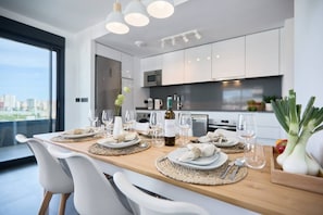 Un comedor moderno con una mesa de madera lista para una comida, sillas blancas y vistas a la ciudad a través de ventanas amplias.