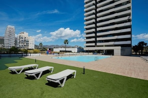 Un área de piscina en la azotea con sillones de descanso, una piscina e imponentes edificios modernos al fondo.