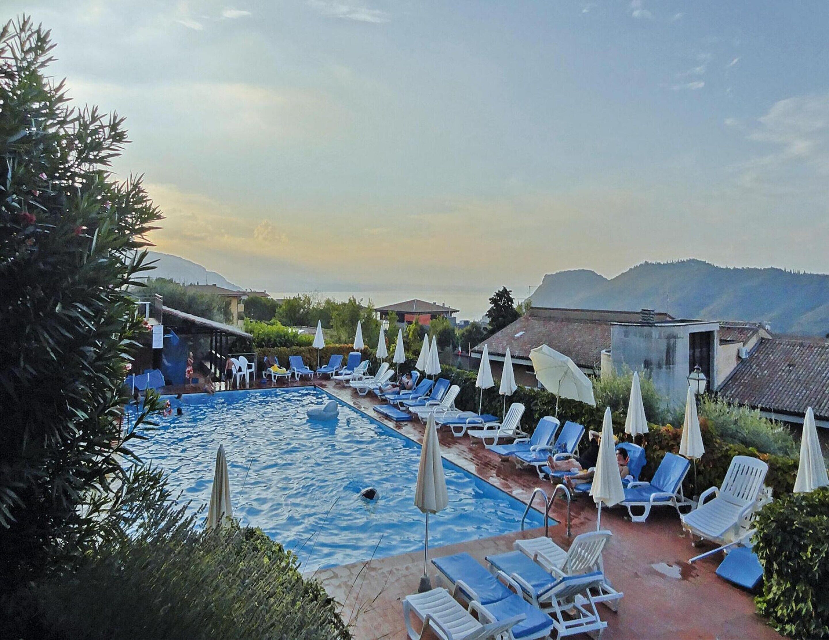 A pool area with lounge chairs and umbrellas, surrounded by greenery and buildings.