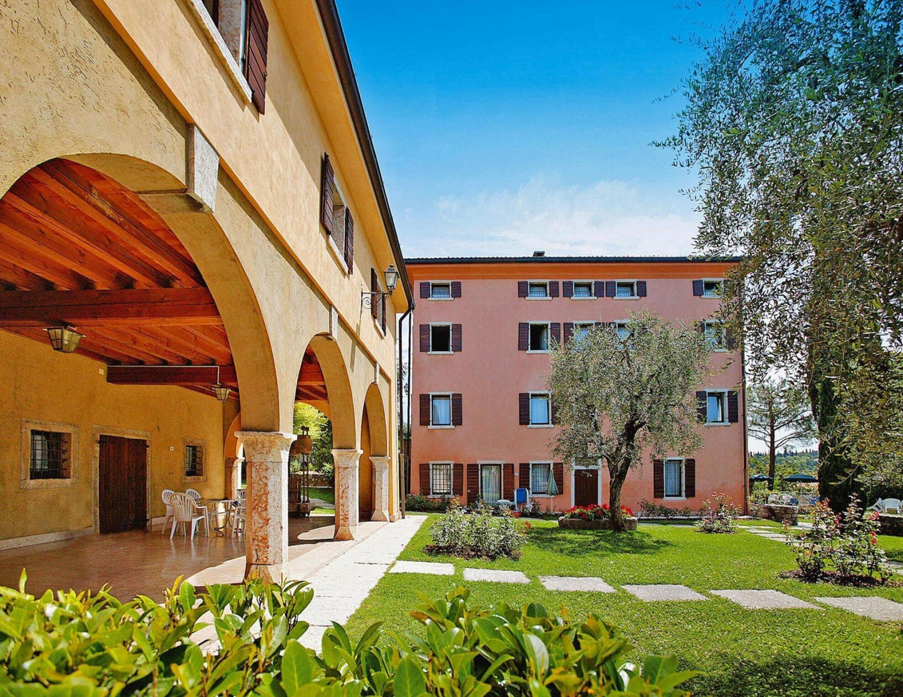 A courtyard with a building featuring arched walkways and a garden area.
