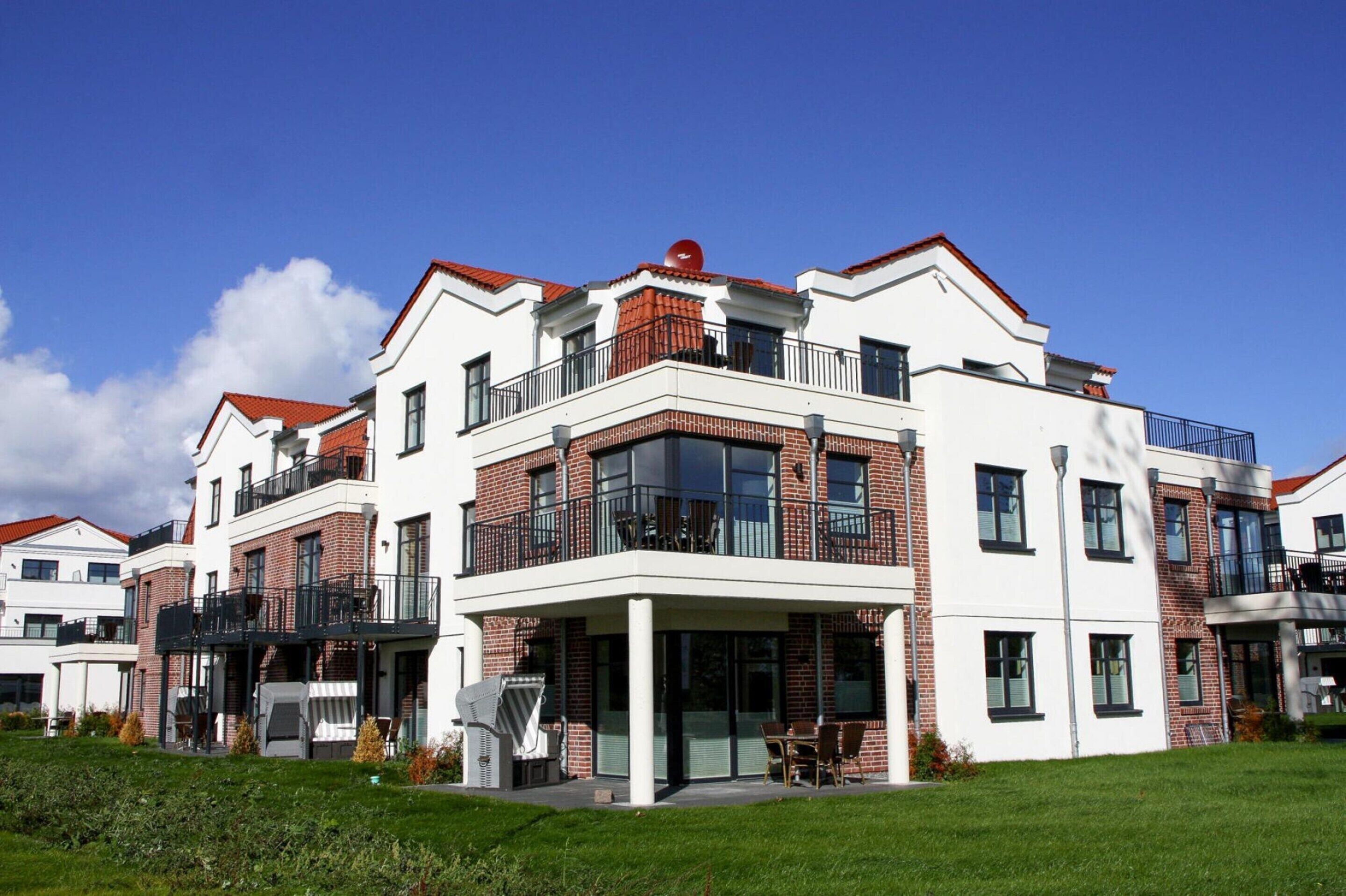 A modern multi-story residential building with a flat roof, large windows, and a covered outdoor area with seating.