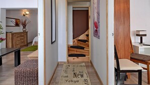 Un intérieur moderne avec un escalier en bois, un coin repas et un couloir agrémenté d’un tapis orné de noms de villes.