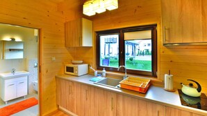 Une cuisine compacte avec des meubles en bois, un four à micro-ondes, une bouilloire et une fenêtre donnant sur un jardin.
