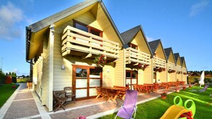 Une rangée de cabanes en bois dotées de balcons, d’un espace extérieur aménagé pour s’asseoir et d’une aire de jeux pour enfants.