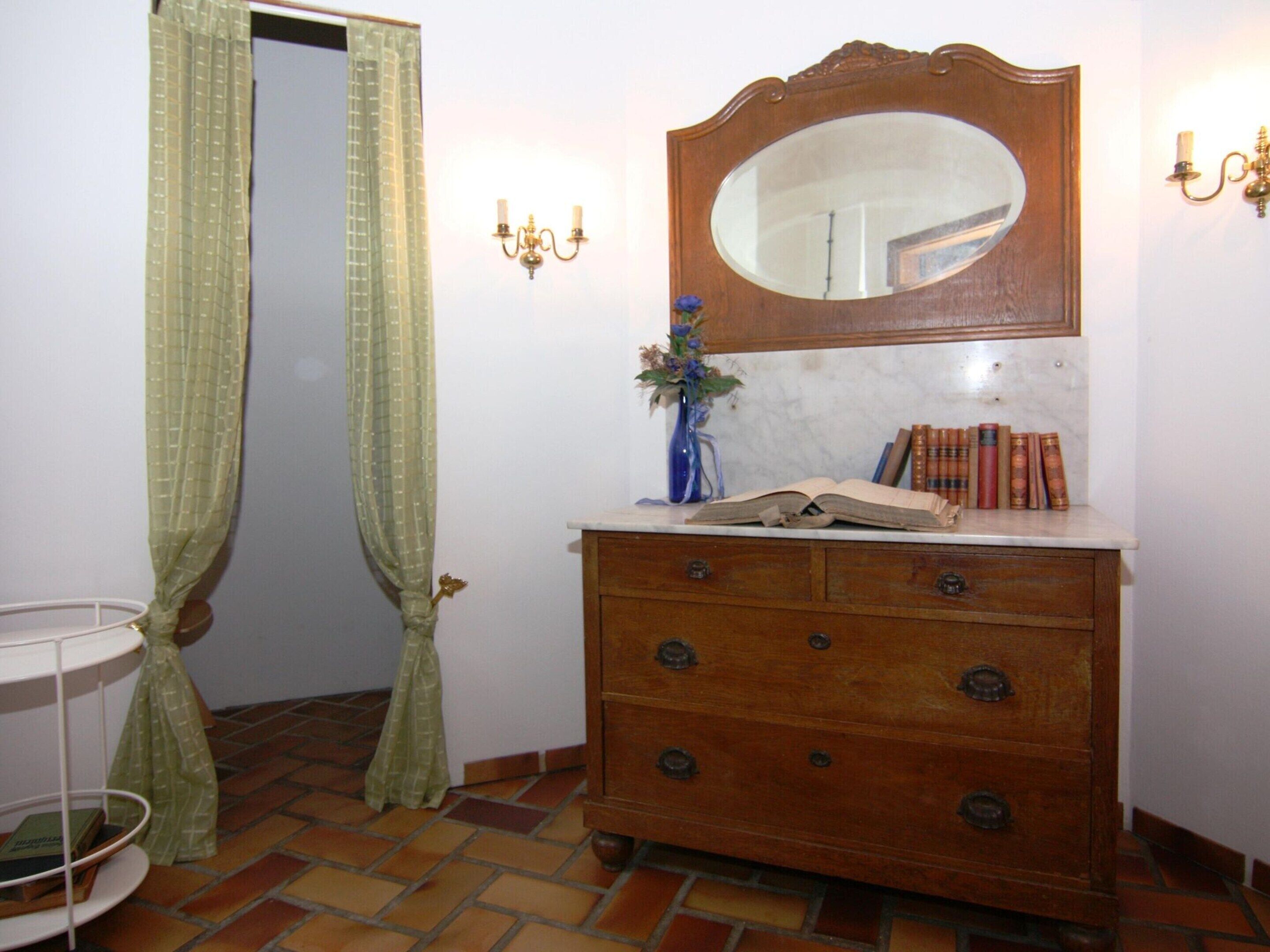 Um banheiro com uma penteadeira de madeira, um espelho, um vaso com flores e uma estante com livros.