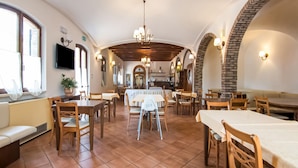 A restaurant with a central dining area, multiple tables and chairs, and a kitchen visible in the background.