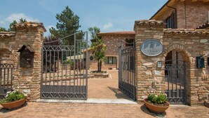 A stone villa with a gated entrance, a sign indicating 'Villa', and a brick pathway leading to the main building.