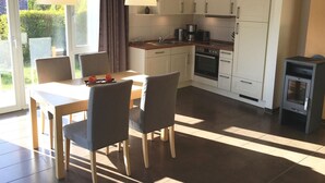 A modern kitchen with white cabinets, a built-in oven, and a stove. There is a dining table with chairs and a pendant light above it. - Ferienhaus Muritzhus an der Muritz (Röbel/Müritz)