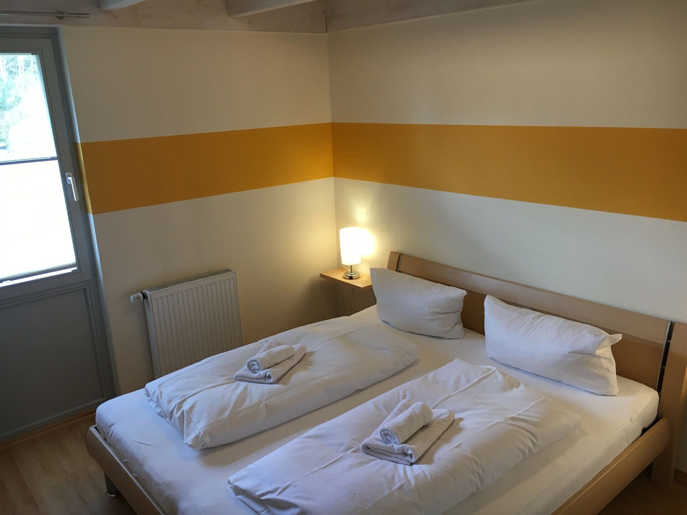 Une chambre d’hôtel avec un lit double, une table de chevet avec une lampe et une fenêtre donnant sur des arbres.