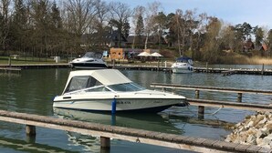 A boat docked at a marina with a wooden pier, surrounded by trees and houses in the background. - Ferienhaus Muritzhus an der Muritz (Röbel/Müritz)