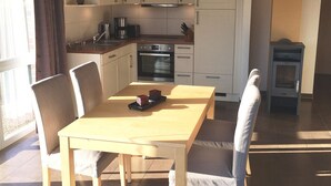 A modern kitchen with white cabinets, a built-in oven, and a coffee maker. There is a dining table with chairs and a small plant on the counter. - Ferienhaus Muritzhus an der Muritz (Röbel/Müritz)