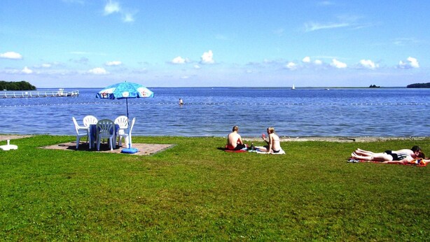A grassy area with a blue umbrella, white chairs, and a small table. - Ferienhaus Muritzhus an der Muritz (Röbel/Müritz)