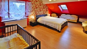 A bedroom with a large bed, a window with curtains, a red wall, a wooden floor, and a small table with a chair. - Comfy Lakeside House With Private Garden (Ińsko)
