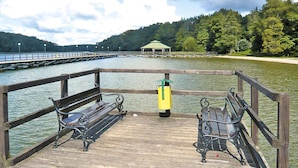 A wooden pier with two benches facing a calm lake, a green gazebo in the distance, and a forested hill. - Comfy Lakeside House With Private Garden (Ińsko)
