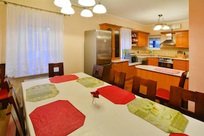 A dining area with a table set for four, a refrigerator, and wooden cabinets in the background. - Comfy Lakeside House With Private Garden (Ińsko)