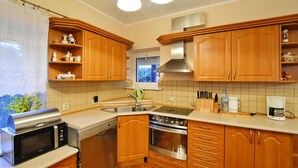 A kitchen with wooden cabinets, a stainless steel microwave, a stove, and a coffee maker. - Comfy Lakeside House With Private Garden (Ińsko)