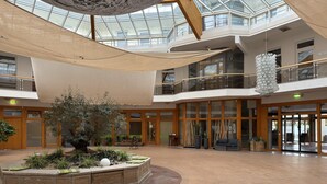 A spacious atrium with a central garden, wooden flooring, and a glass ceiling. - Residence Park am Schweriner See, Schwerin (Raben Steinfeld)