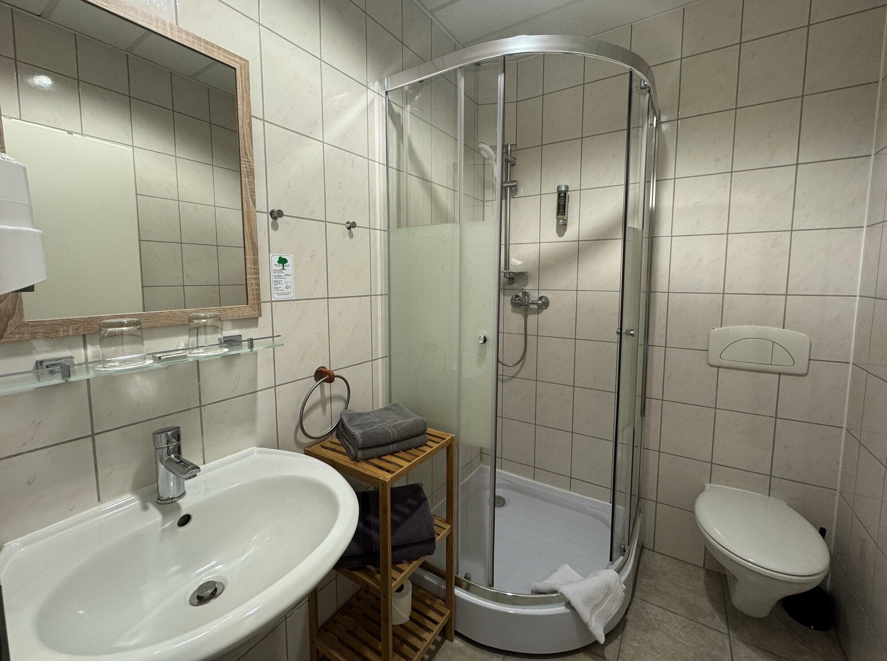 Un baño con lavamanos, inodoro y cabina de ducha con mampara de vidrio.