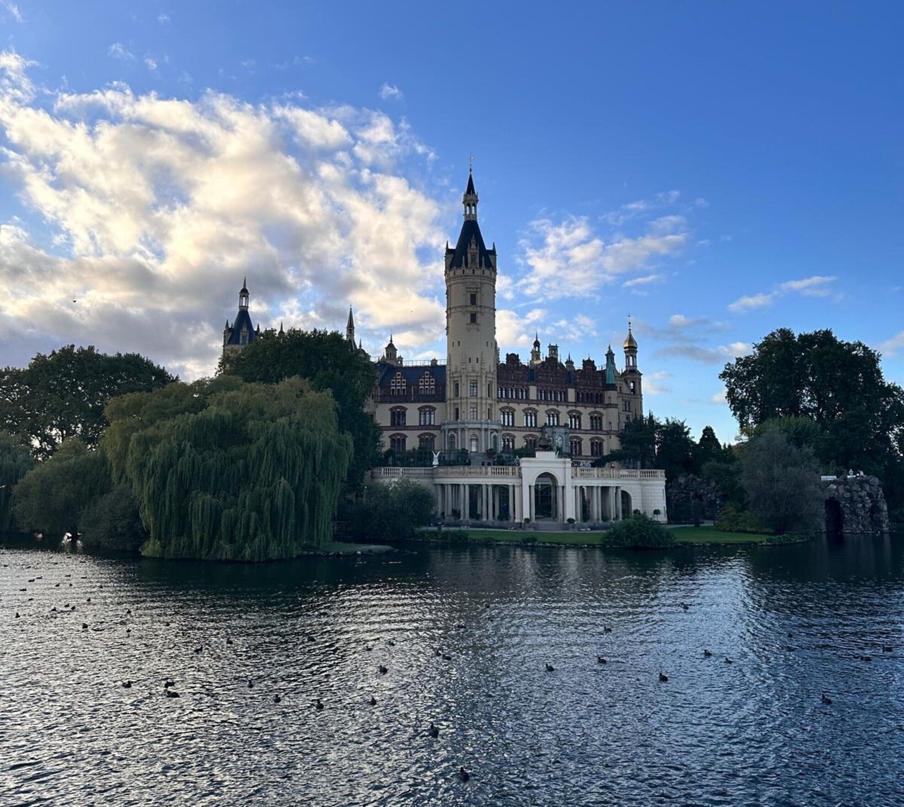 Un grand bâtiment historique, doté d’une tour imposante, situé au bord d’un lac paisible.