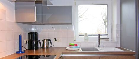 Eine moderne Küche mit Einbauherd, einer Kaffeemaschine und einem Fenster mit Blick auf Bäume.