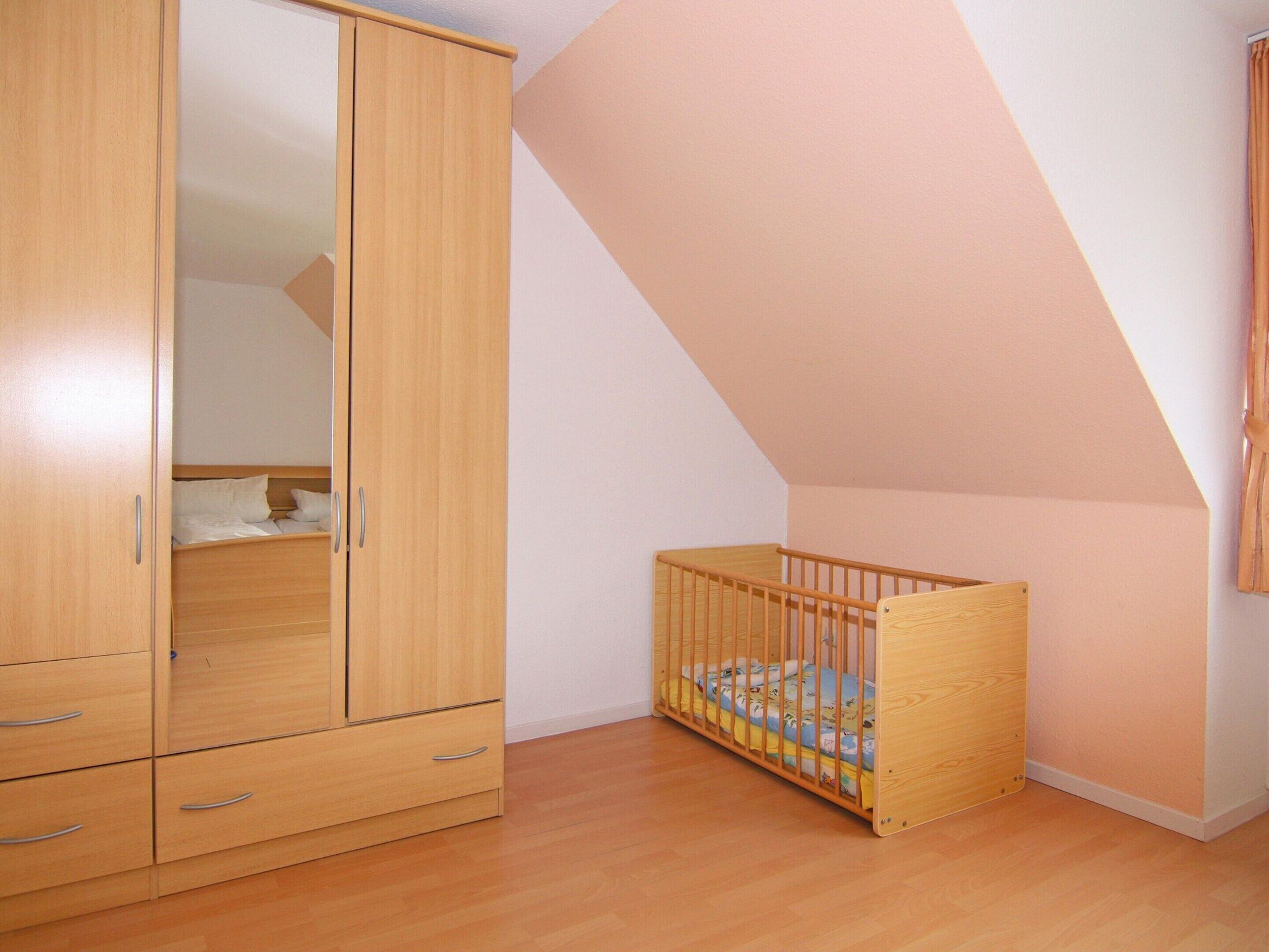 Un dormitorio con un armario de madera, una cuna y un techo inclinado.