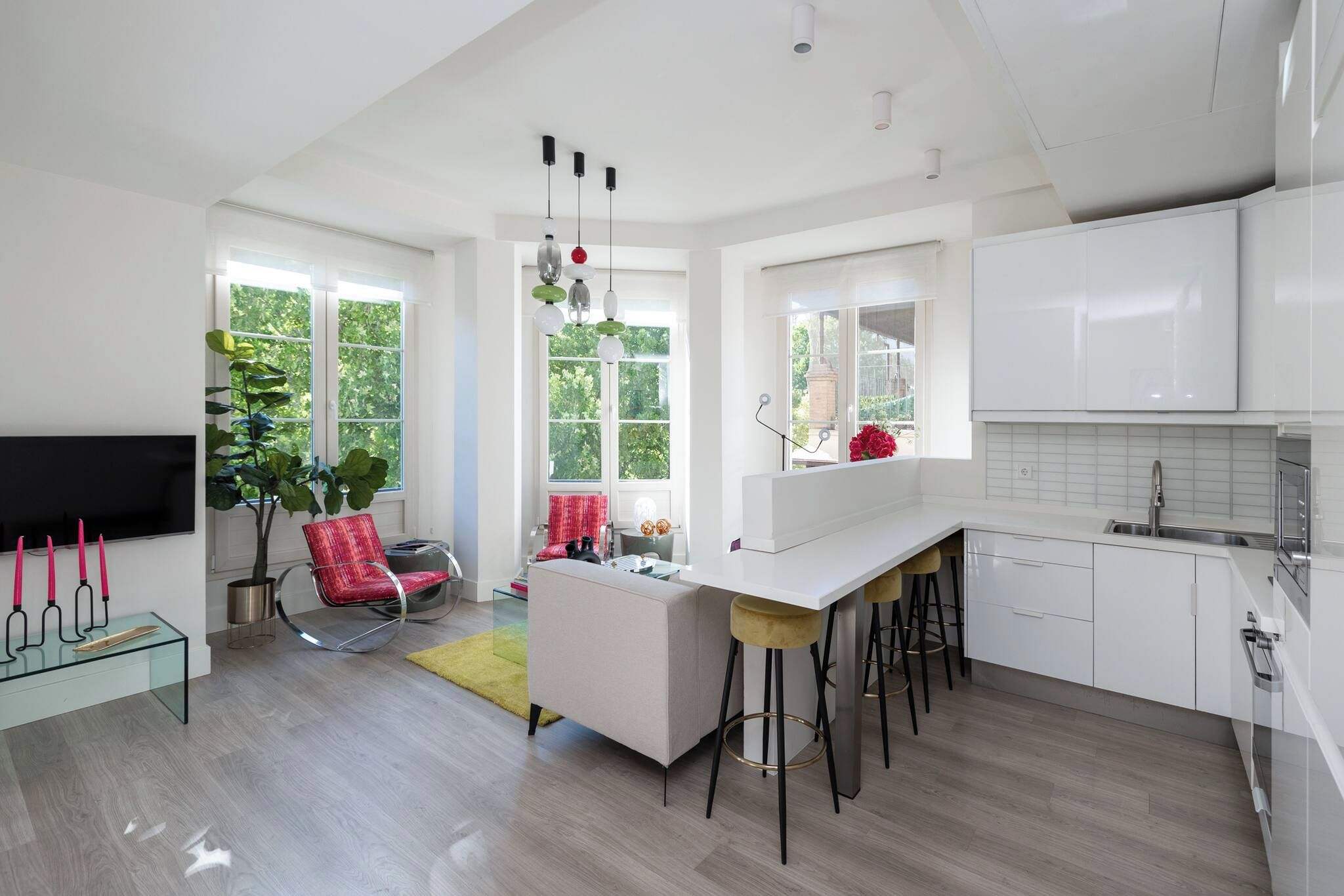 A modern kitchen with white cabinets, a central island with stools, and a dining area with a red chair and a glass table.