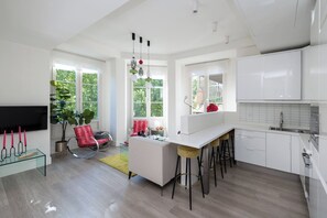 A modern kitchen with white cabinets, a central island with stools, and a dining area with a red chair and a glass table. - Art Suite Granada (Granada)