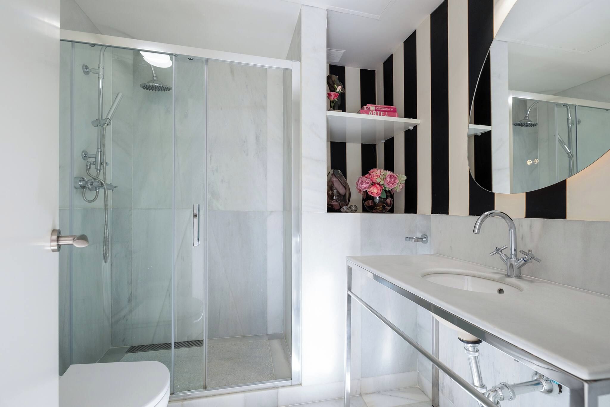 Une salle de bain moderne avec une douche à parois de verre, un lavabo blanc et un grand miroir.