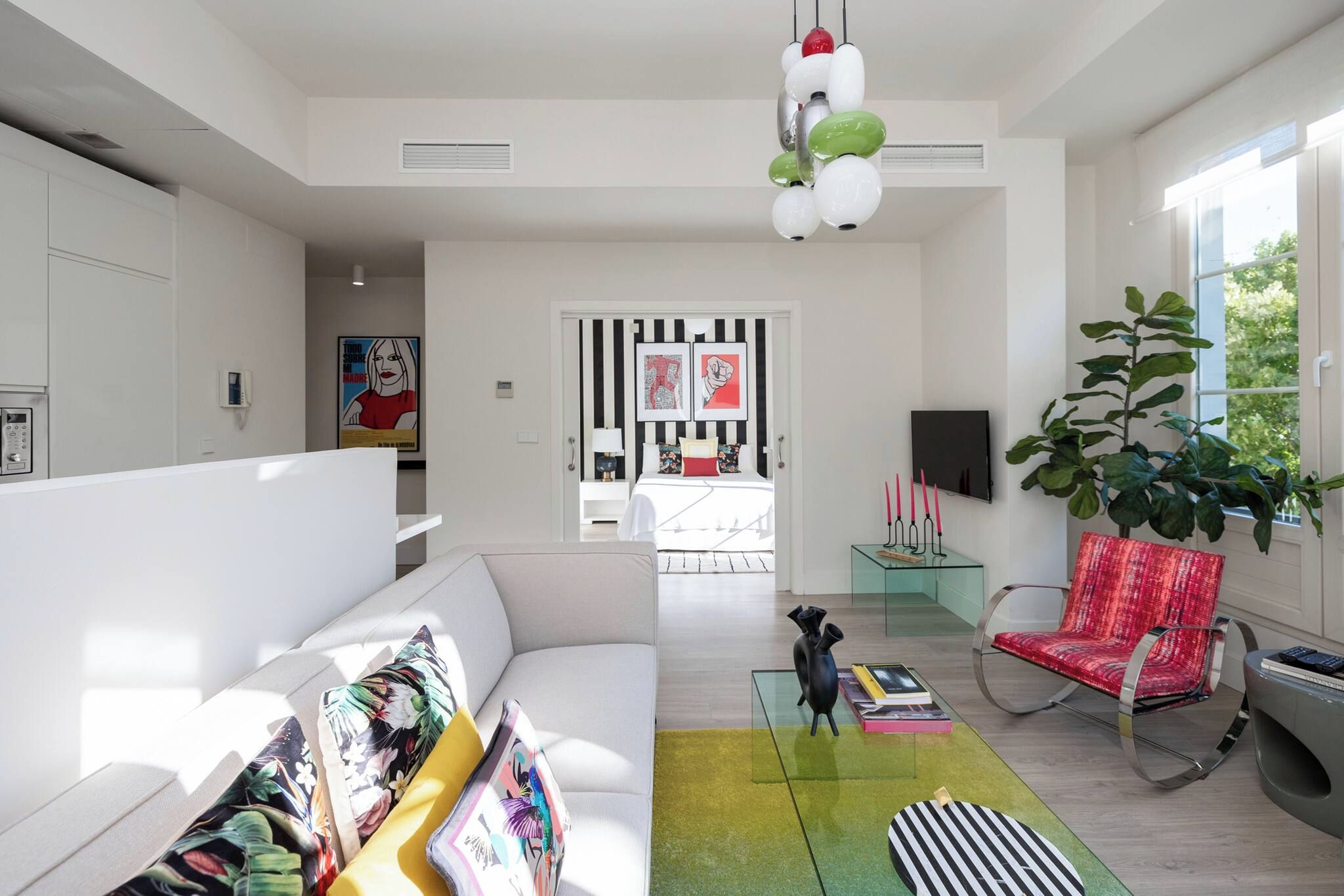 Een moderne woonkamer met een bank, een rode fauteuil, een glazen salontafel en een grote plant.