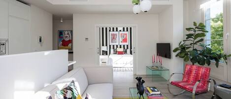 A modern living room with a sofa, a red chair, a glass coffee table, and a large plant.