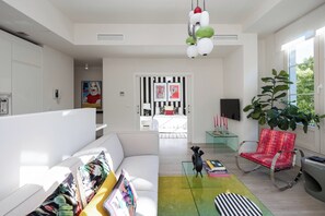 Una sala de estar moderna con un sofá, una butaca roja, una mesa de centro de vidrio y una planta grande.