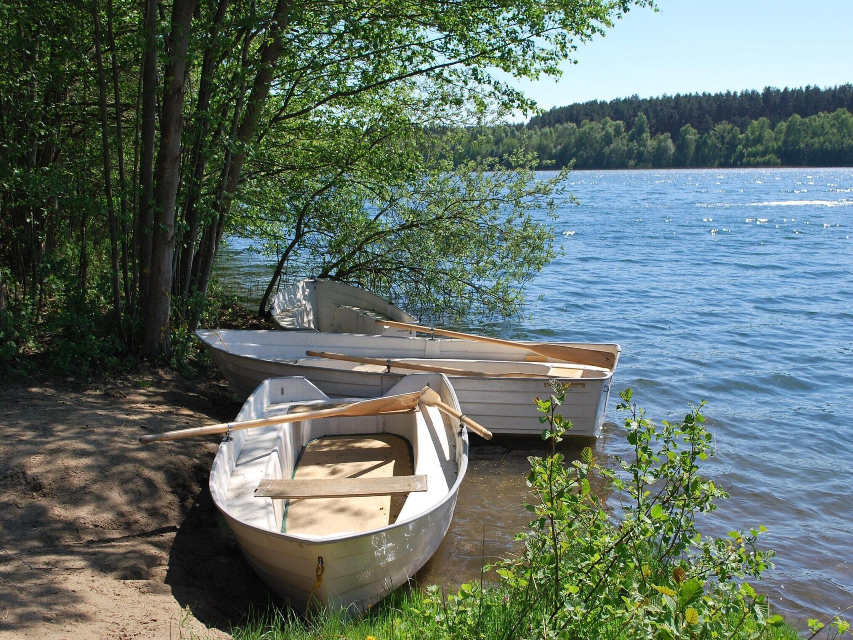 Dos botes amarrados a una orilla arenosa, con un bosque al fondo y un lago.