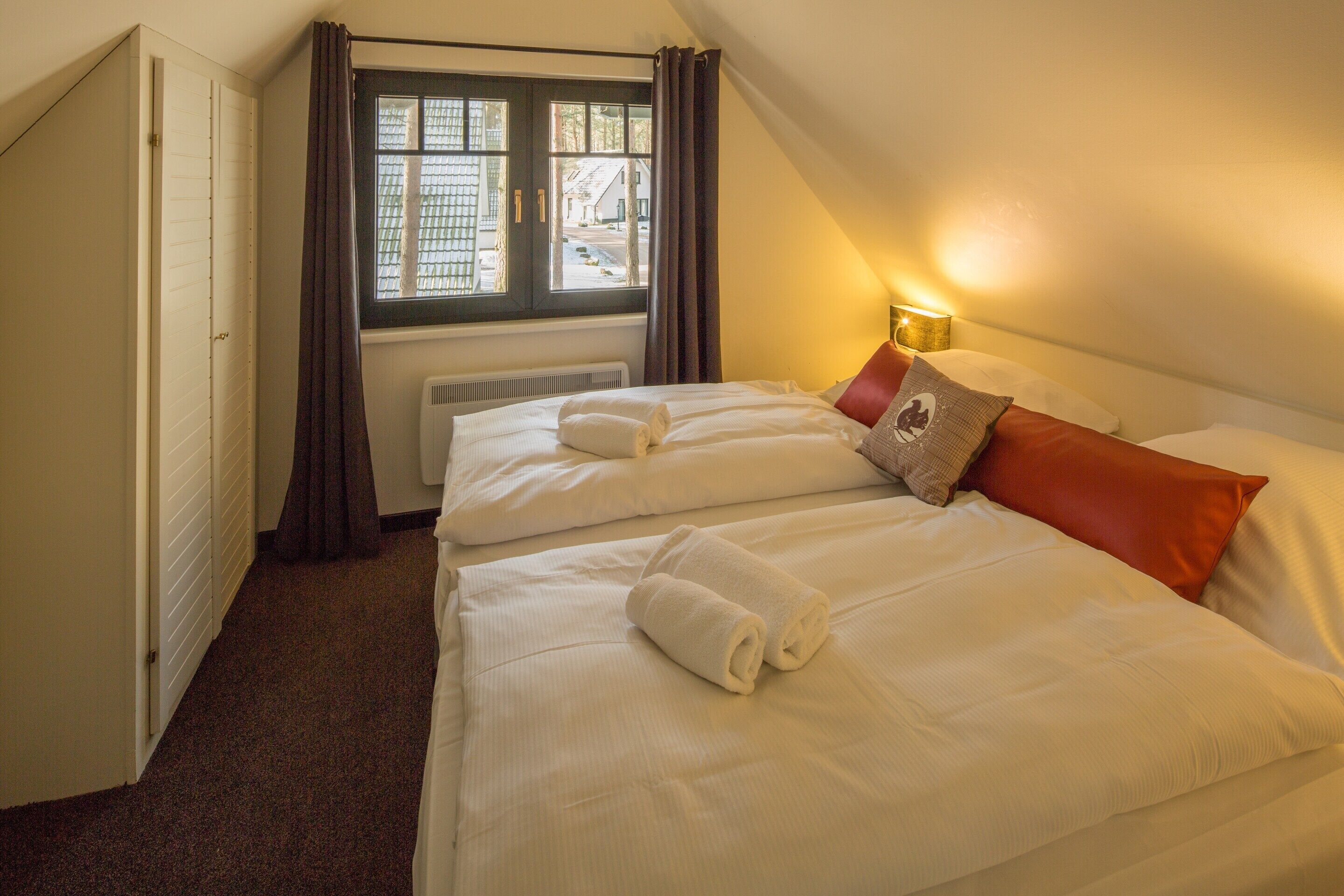 Ein Hotelzimmer mit zwei Betten, einem Fenster mit Vorhängen, einem Heizkörper und einer Nachttischlampe.