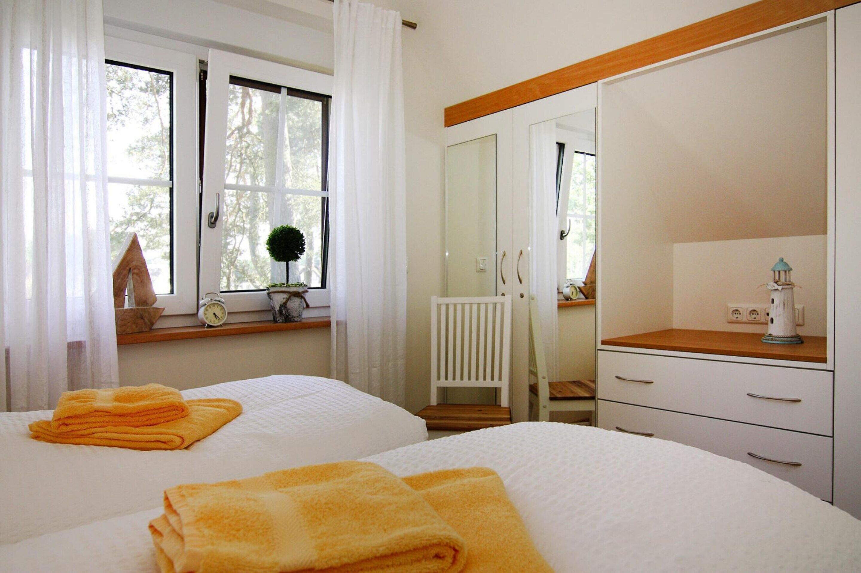 A hotel room with two beds, white bedding, a wooden headboard, a white wardrobe, a small table with a lamp, and a window with curtains.