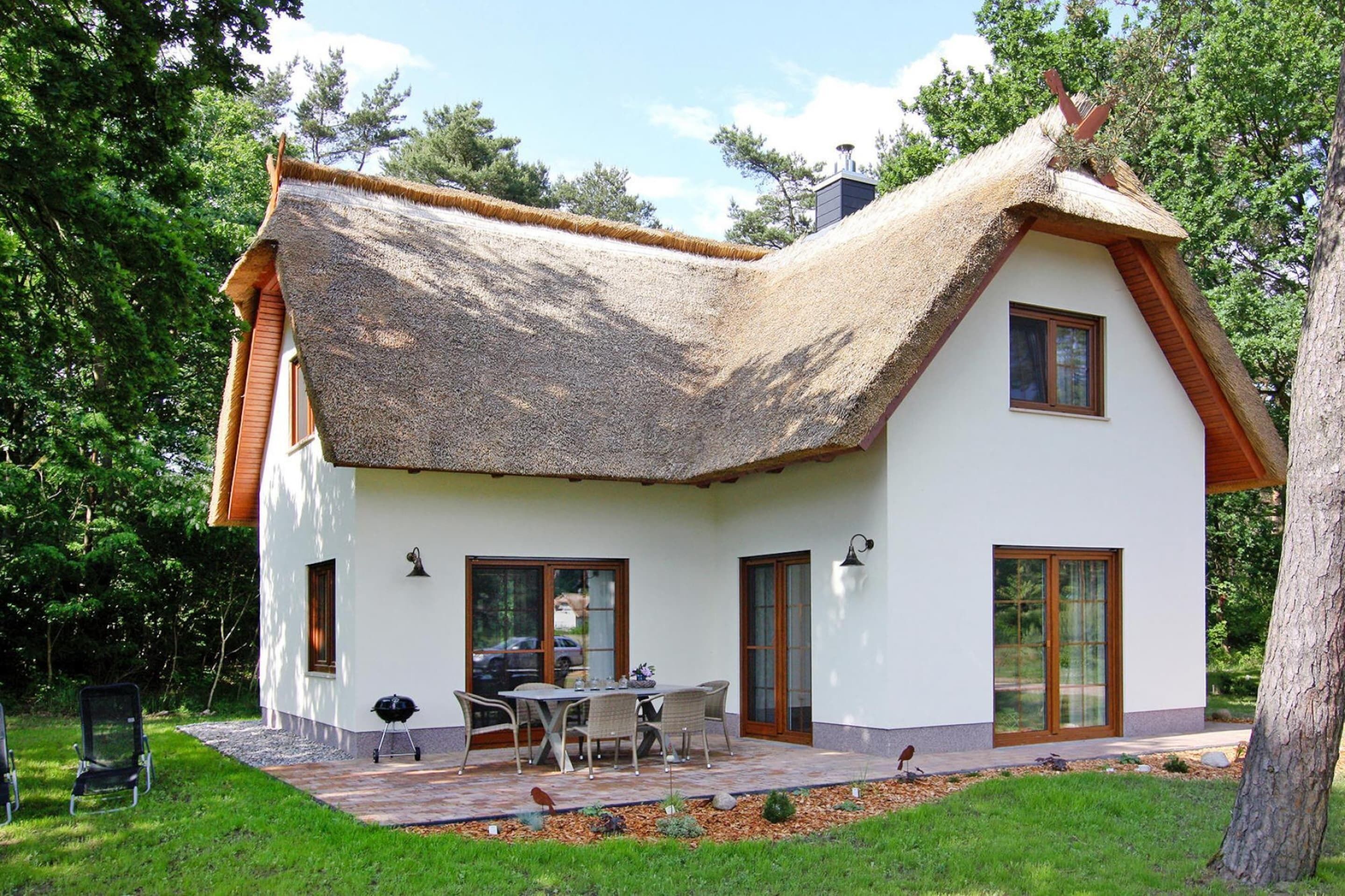 Ein Haus mit einem Strohdach, weißen Außenwänden und einer Terrasse mit Gartenmöbeln.