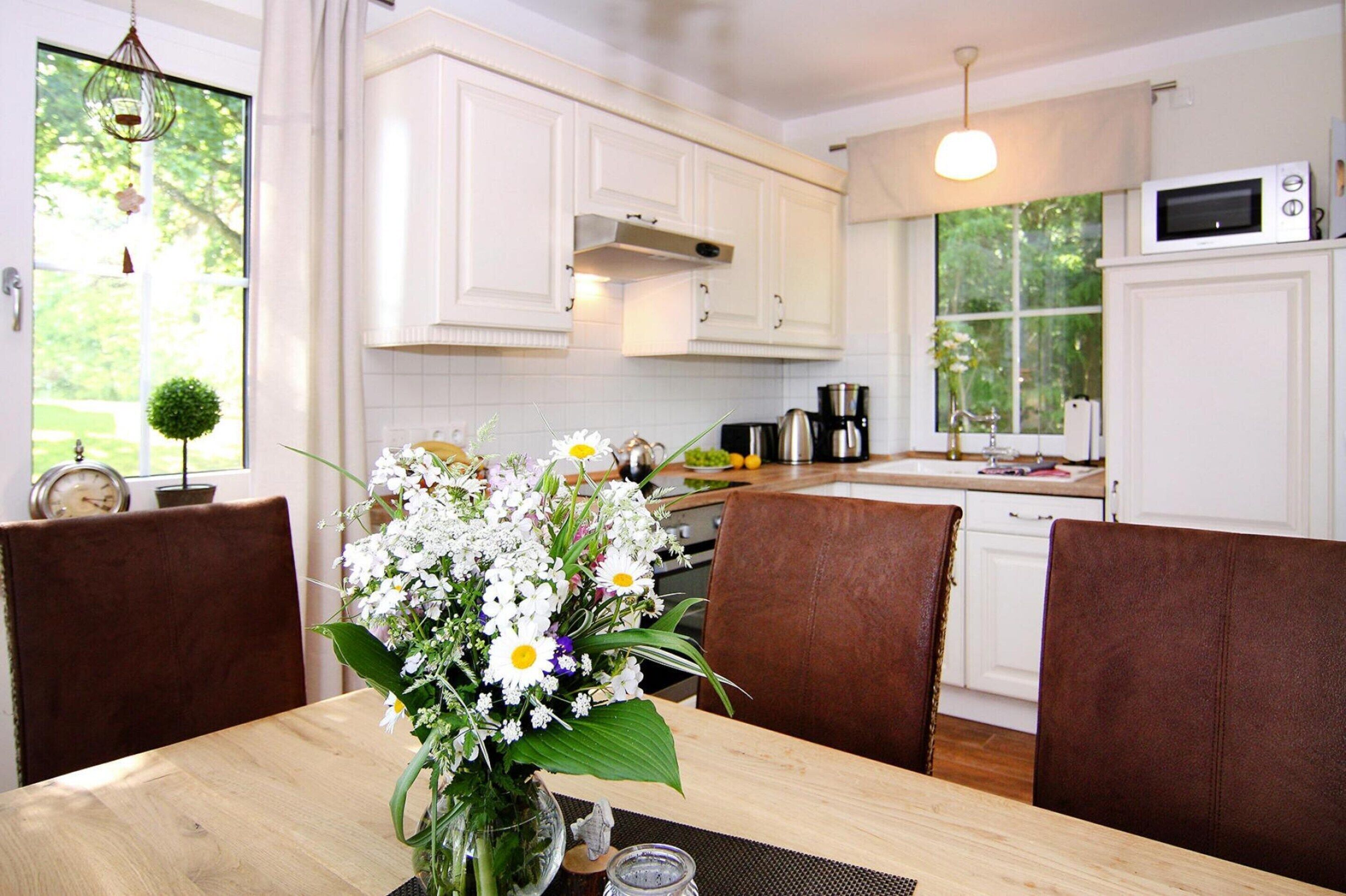A kitchen with white cabinets, a dining table with chairs, and a vase of flowers on the table.