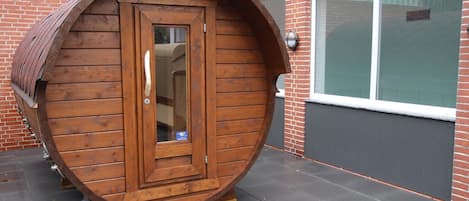 A wooden barrel-shaped structure with a door and a window, placed on a paved surface.